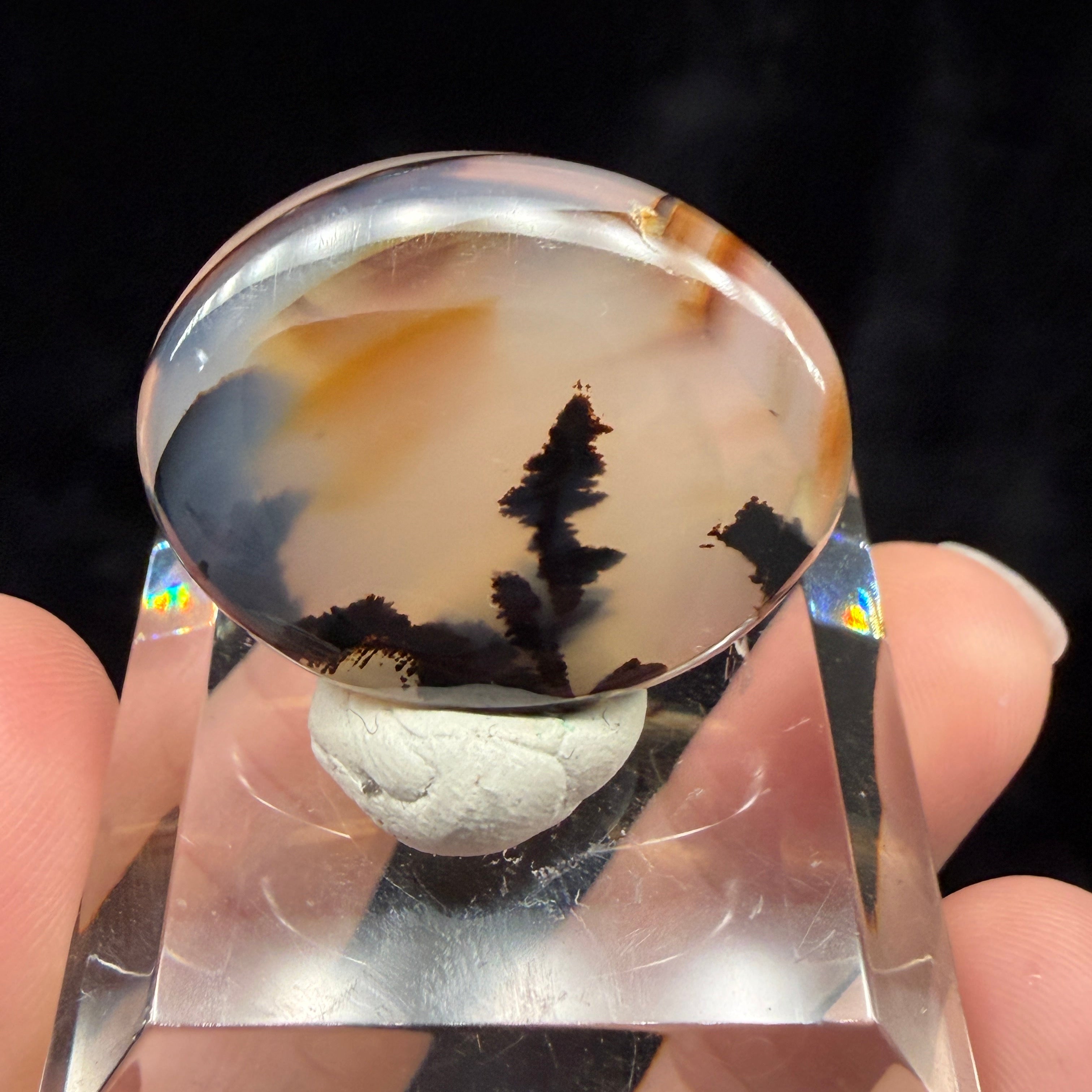 Clear crystal with embedded stone held by a hand against a dark background