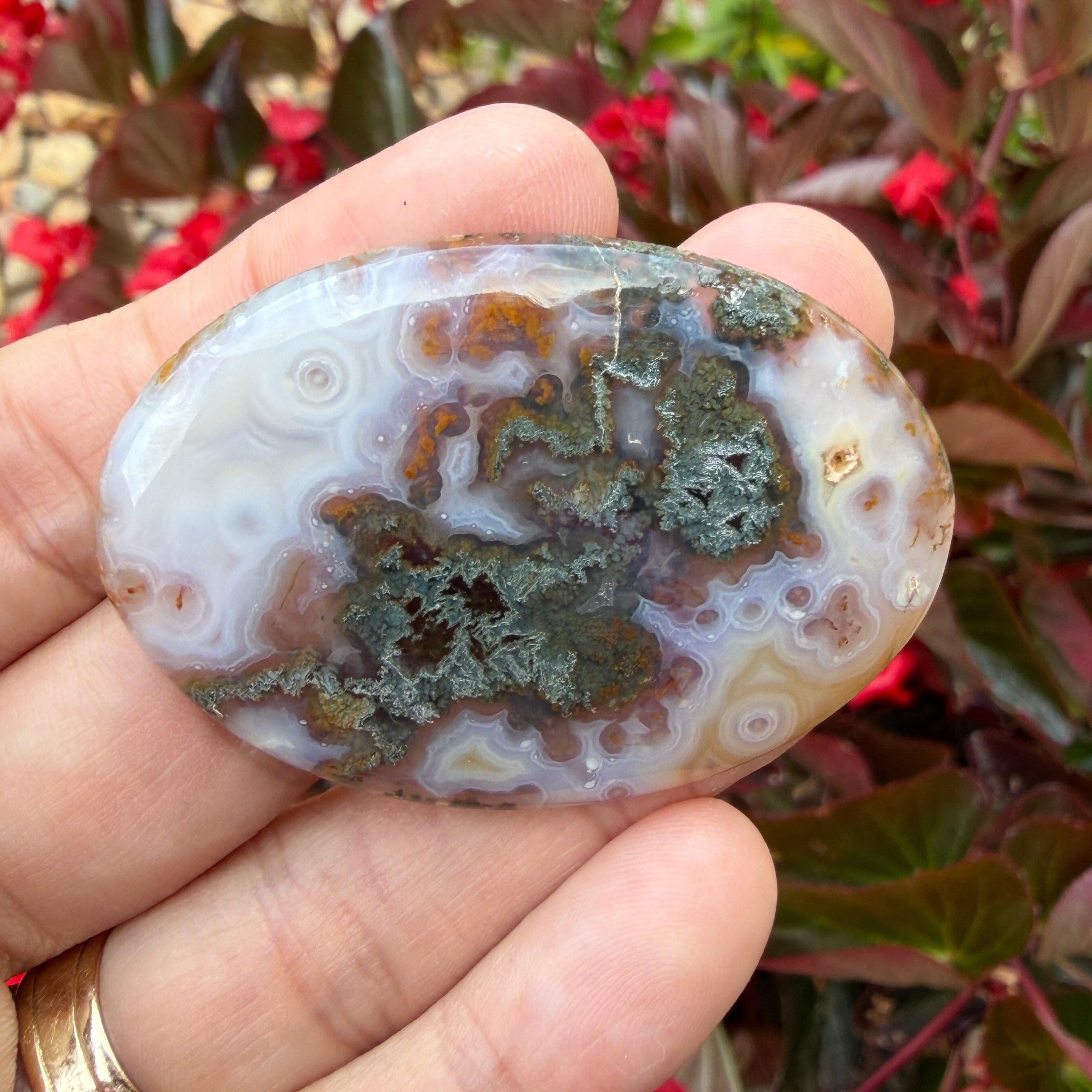 Hand holding a polished agate stone with a floral background