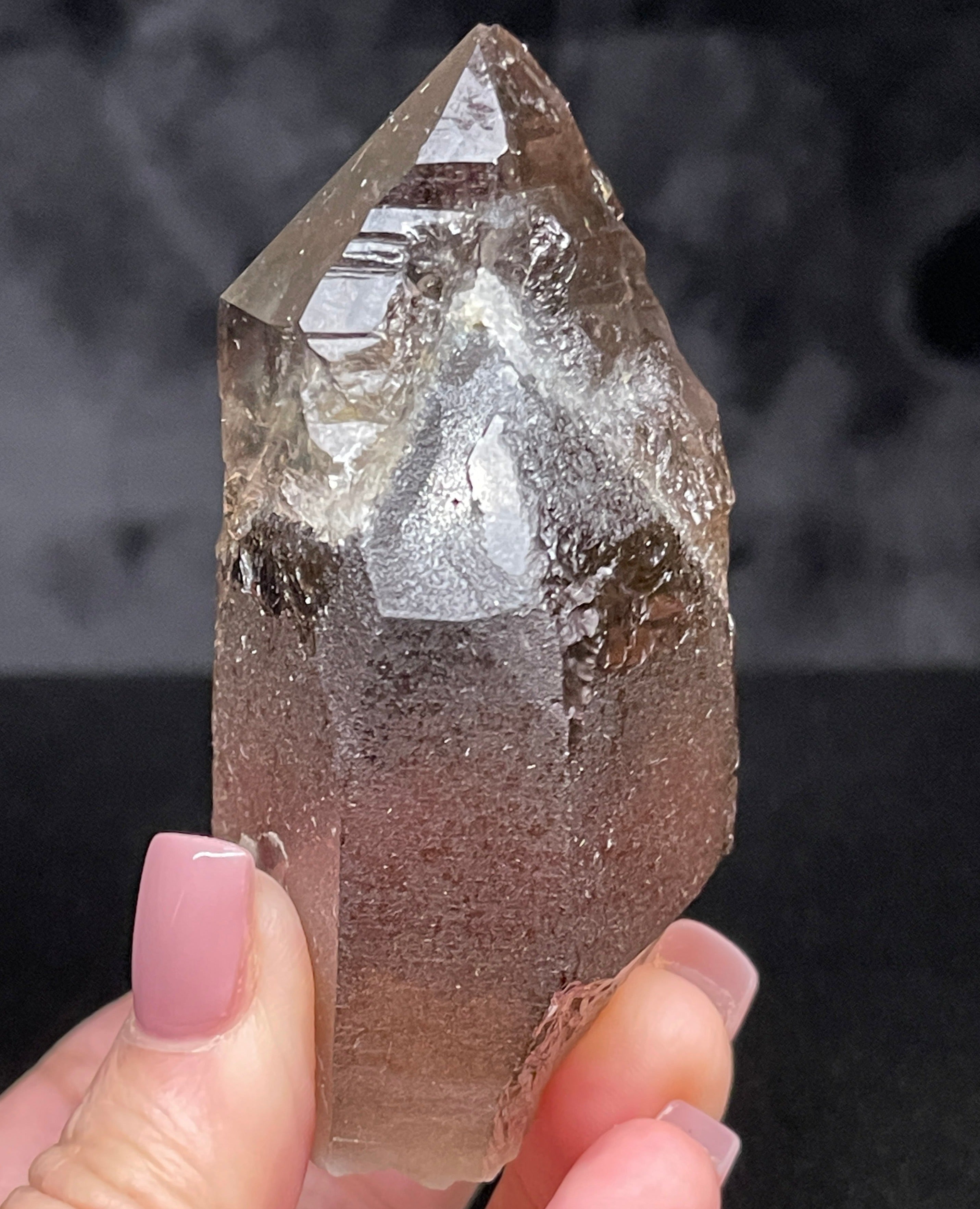 This is Smoky Quartz that exhibits some fascinating complexity in that it shows water clear secondary growth Quartz that grew on or over another darker, almost root beer colored Quartz crystal.