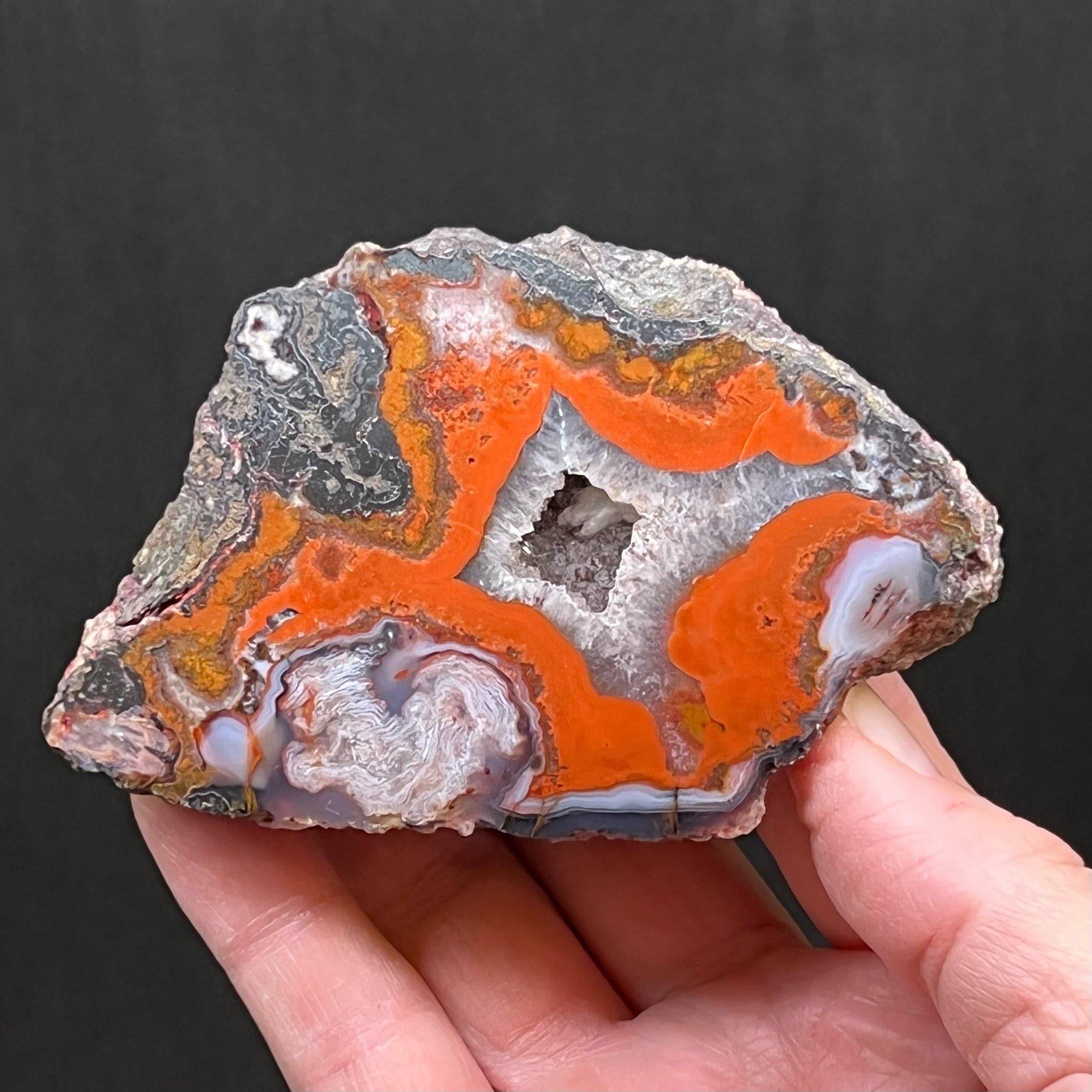 This is an excellent, red-orange color dominate, quality Moroccan Agate specimen with a polished face that presents with banding, an attractive crystalline pocket and hematite along a large part of the edge of the agate.