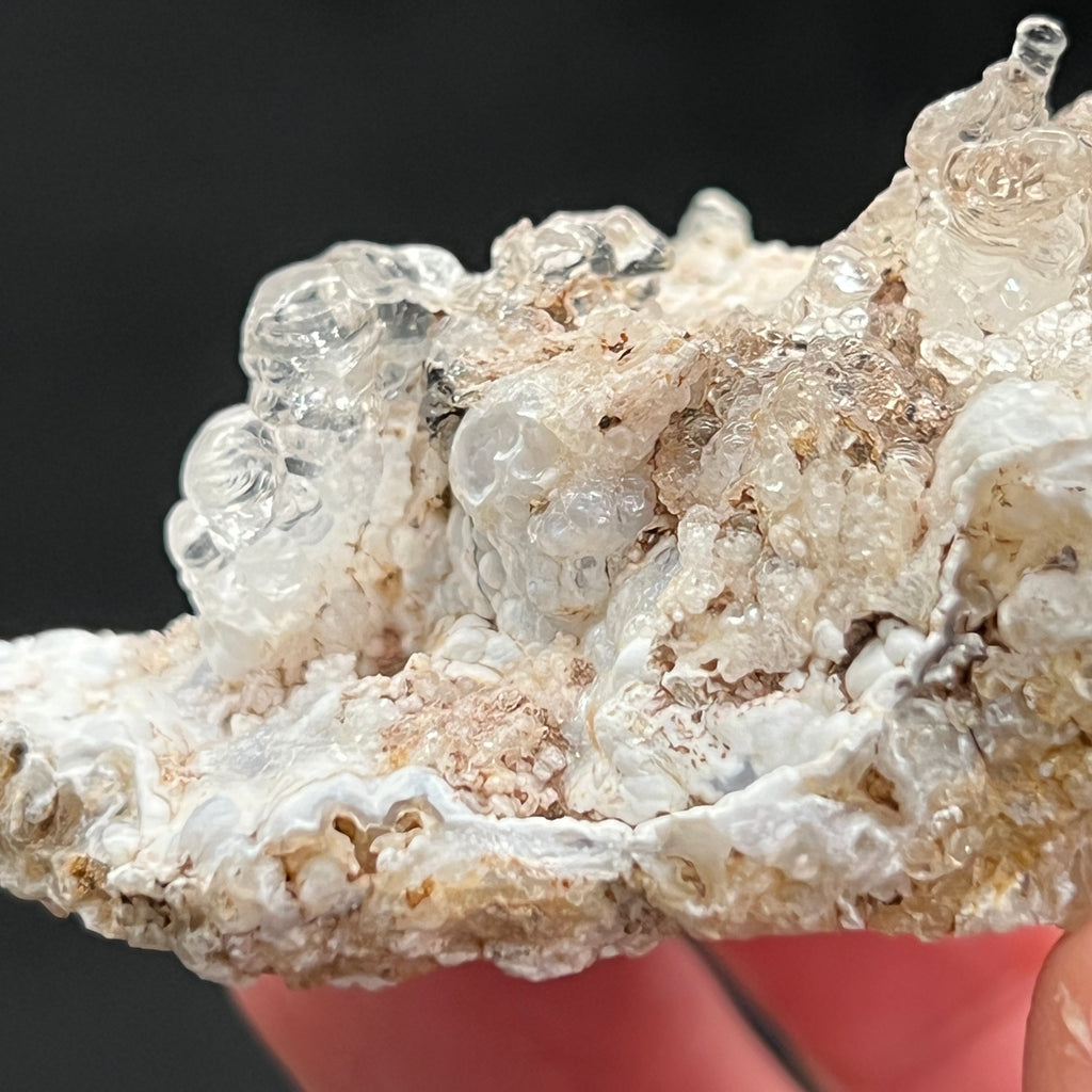 With highest respect to protecting and presenting the natural state of the crystals, it is normal that there remains small amounts of sediment or Rhyolite tuff trapped within and in between the Hyalite spherules. This is truly an excellent example of the species!  