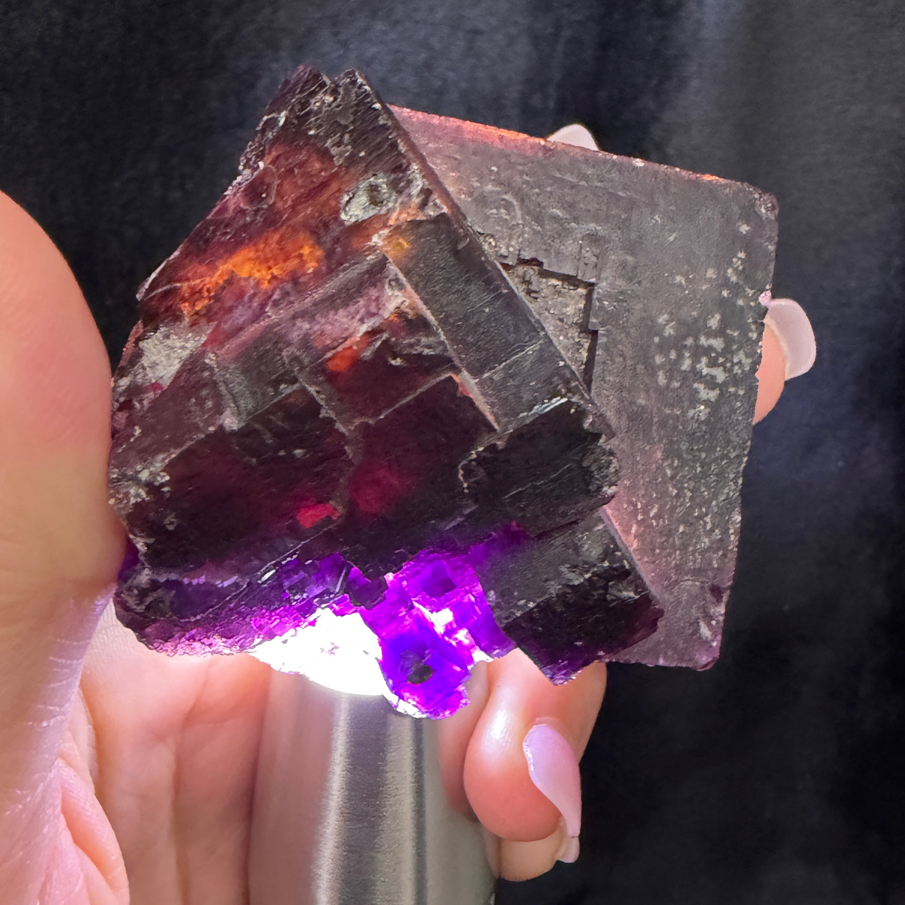 Mineral sample being illuminated by a UV light held in a hand against a dark background