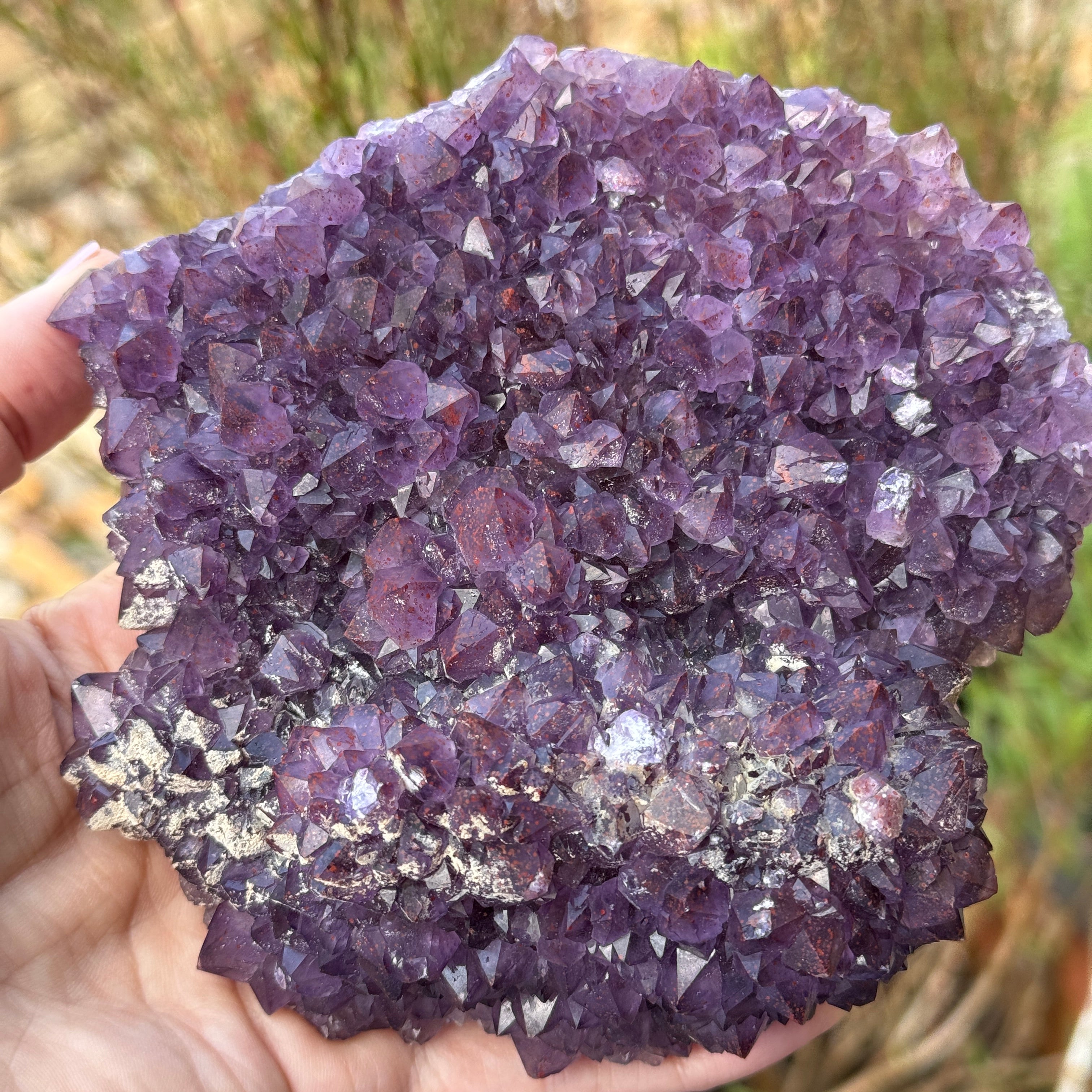 Hand holding a large purple crystal cluster outdoors